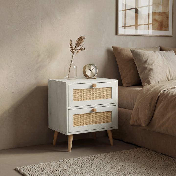 [White] Bedroom scene with Wovena rattan bedside next to brown bedding, vase and gold clock on top under wall art